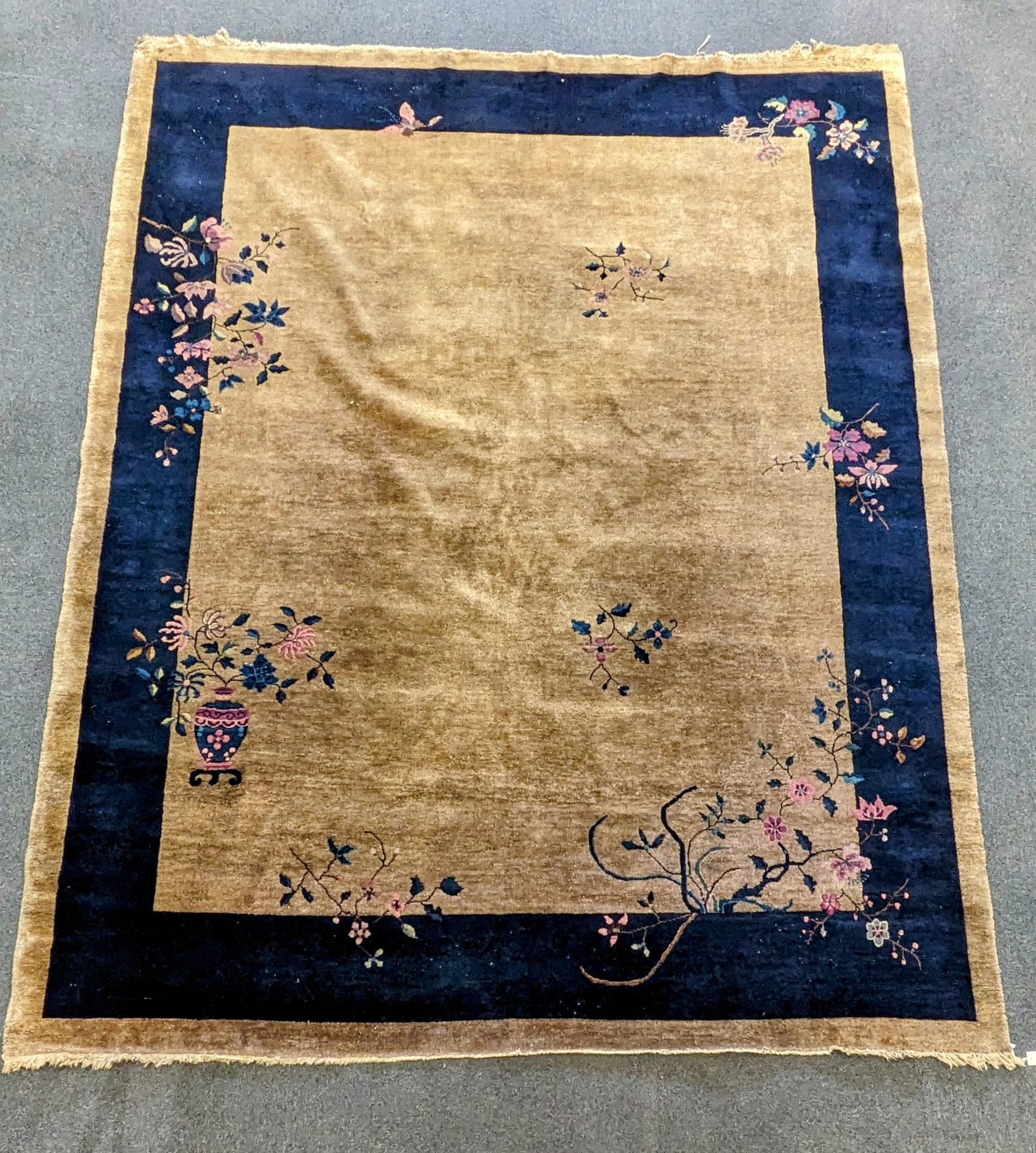 A Walter Nichols Chinese champagne ground carpet with asymmetrical decoration of flowers and an urn, single dark blue border, 350 x 280cm. Condition - fair